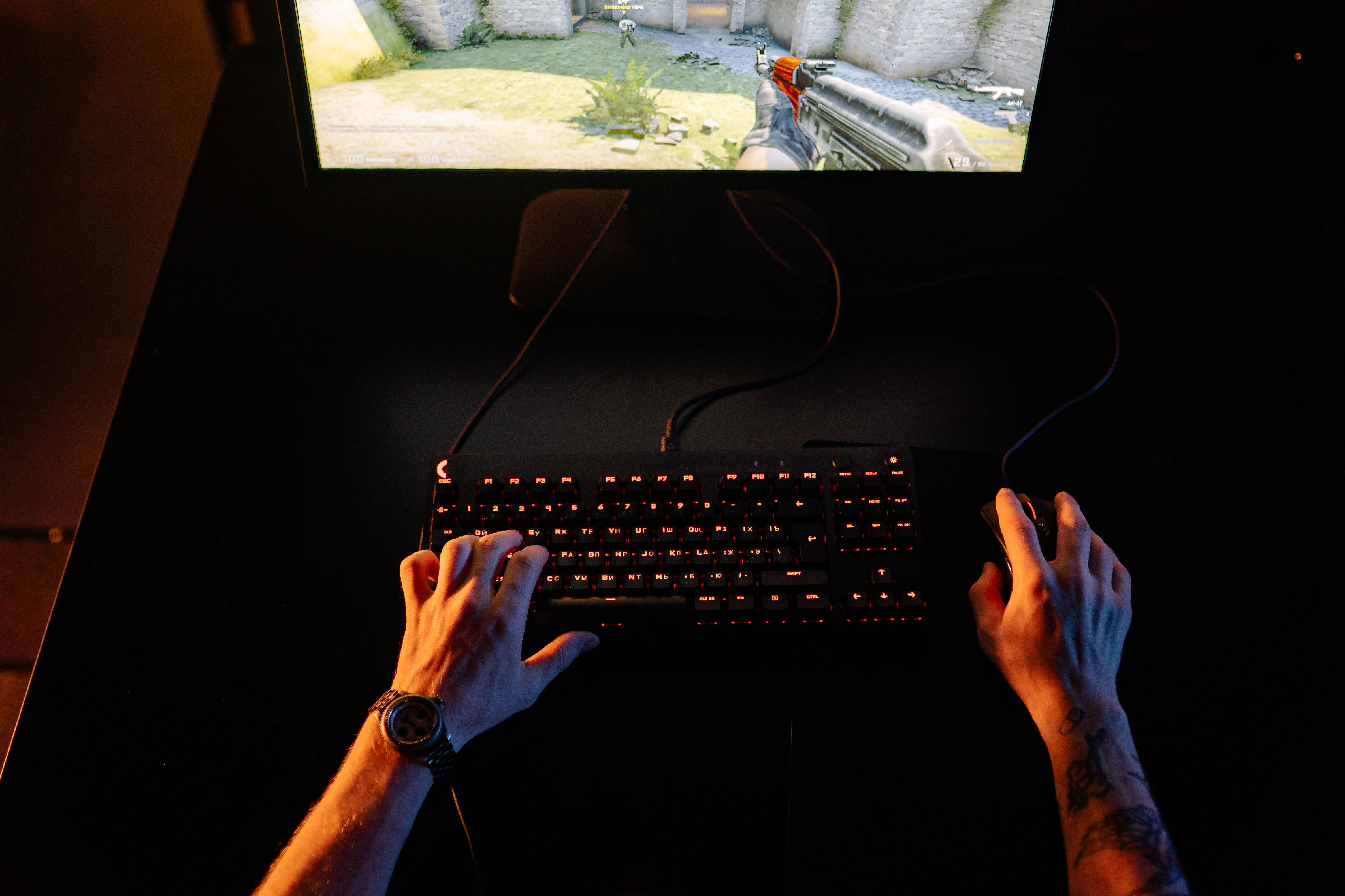 Gamer intensely playing a first-person shooter on a computer setup at night with a gaming headset